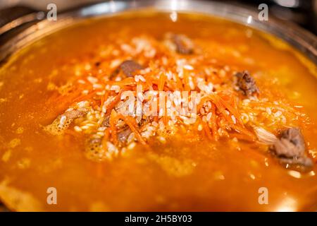 Lammfleisch Kochen mit Karotten auf Bratpfanne mit Reis als traditionelle kasachische oder usbekische Pilaf oder Plov Makro Nahaufnahme mit oranger Farbe Stockfoto