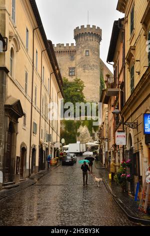 Borgo di Bracciano e Castello Orsini-Odescalchi-Eine Straße der Stadt Bracciano und im Hintergrund einer der Türme des imposanten Schlosses. Stockfoto