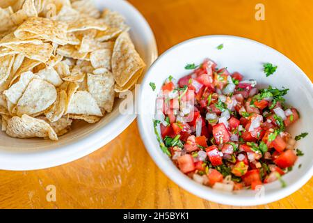 Nahaufnahme von klobigen roten Salsa aus roten Tomaten, süßer Zwiebel und Koriander mit frittierten gelben Mais-Tortilla-Chips auf weißem Teller, hausgemachter mexikanischer Stockfoto