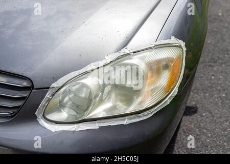 Auto-Auto-Fahrzeug vorne nebligen schmutzigen Scheinwerfer mit Schutzband um das Licht geklebt, um Farbe für die Reinigung Polieren zu Hause Auffahrt des Hauses zu schützen Stockfoto