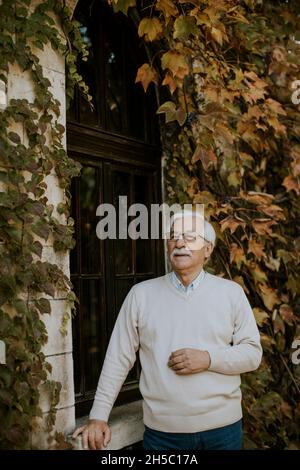 Gesunder älterer Mann, der am Herbsttag am Fenster steht Stockfoto
