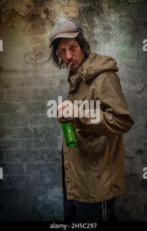 Junkie Mann mit Mütze grün Anorak und blaue Jogginghose in der Nähe Stein alten Wand Stockfoto