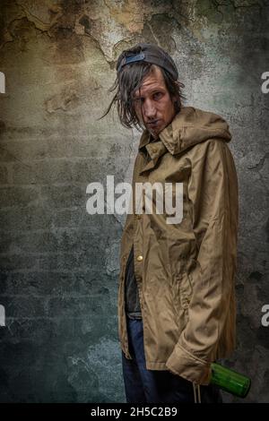 Junkie Mann mit Mütze grün Anorak und blaue Jogginghose in der Nähe Stein alten Wand Stockfoto