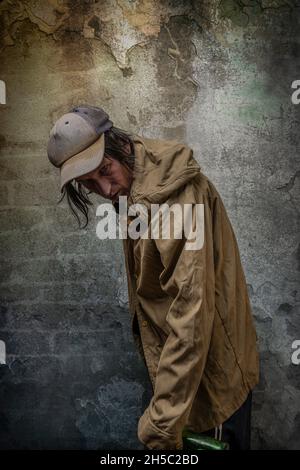 Junkie Mann mit Mütze grün Anorak und blaue Jogginghose in der Nähe Stein alten Wand Stockfoto