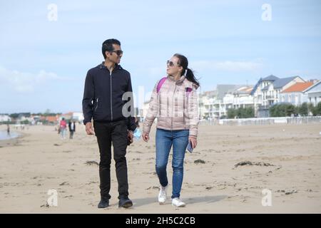 Lächelndes Paar, das am Strand, am Chatelaillon-Strand, in der Charente Maritime, in der Nouvelle-Aquitaine, Frankreich, spazieren geht Stockfoto