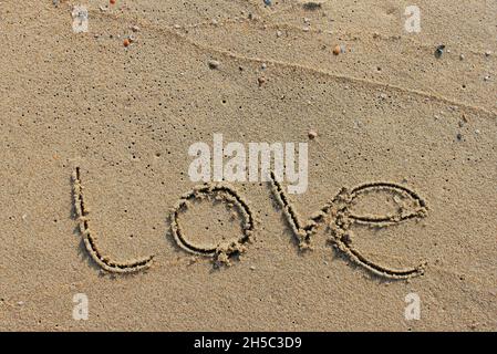 Am Strand ist mit Buchstaben in den glatten Sand die Schrift Liebe geschnitzt Stockfoto