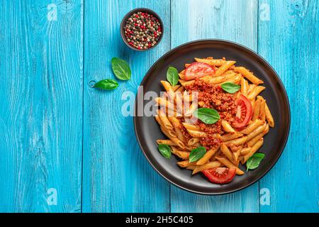 Pasta Penne mit Bolognese-Sauce und Basilikum auf einem schwarzen Teller auf blauem Hintergrund. Italienische Küche. Stockfoto