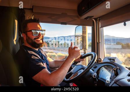 Schwerer Lkw-Fahrer glücklich, in der Lage sein, einen LKW zu fahren, und macht die Geste der OK, mit dem Daumen nach oben. Stockfoto