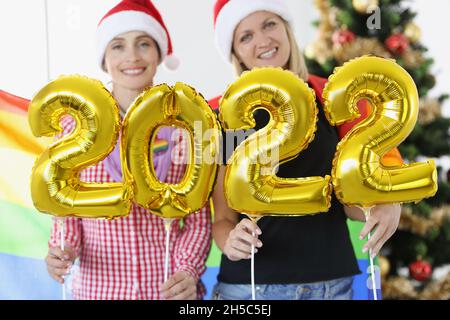 Zwei Frauen mit weihnachtsmannmützen halten die Zahlen 2022 vor dem Hintergrund des Neujahrsbaums Stockfoto