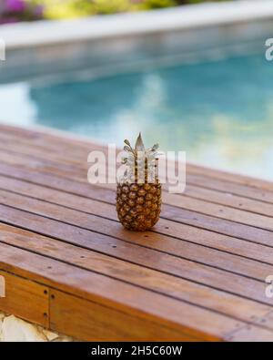 Vertikale Aufnahme einer Ananas auf einer hölzernen Bank in der Nähe eines Pools Stockfoto