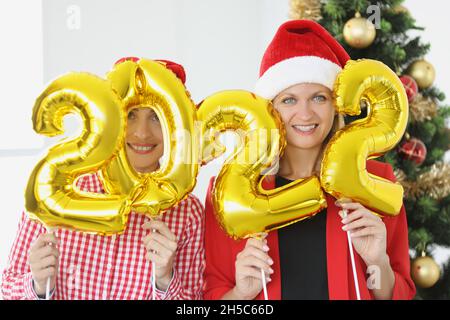 Porträt von zwei jungen Frauen, die die Zahlen 2022 in den Händen gegen den Neujahrsbaum halten Stockfoto