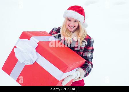 Winter Frau mit Geschenk. Christmas Girl hält ein großes Geschenk. Verrückte Weihnachten Mädchen schiebt ein großes Geschenk auf Schnee Winter Hintergrund. Frohe Weihnachten und glücklich Stockfoto