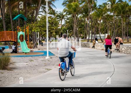 Miami Beach, USA - 17. Januar 2021: Menschen, die auf dem Ocean Walk auf dem Lummus öffentlichen Park am Ocean Drive im Art-Deco-Viertel von South Fahrrad fahren Stockfoto