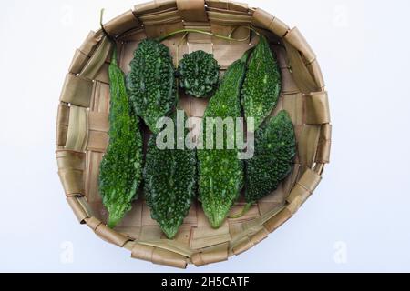 Bittergourd oder Bittermelonen im Korb gestapelt. Grünes Gemüse verschiedene Größen von Karela in Weidenkorb mit holzigen Hintergrund Stockfoto