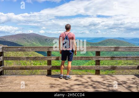 Ein junger Mann mit Rucksack mit Kordelzugbeutel, der auf der Aussichtsplattform steht, überblickt die Holzplattform im Wintergreen-Skiresort in der Natur der Highlands le Stockfoto
