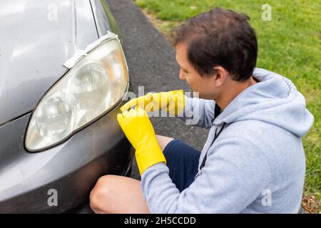 Mann Person Arbeiter setzen Handschuhe an für die Reinigung Auto schmutzig nebligen Scheinwerfer geklebt, um Farbe auf der Zufahrt des Hauses draußen zu schützen Stockfoto