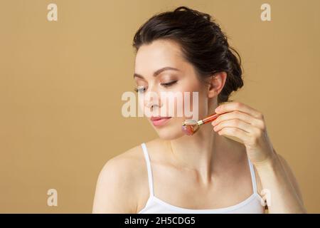 Porträt einer jungen Frau mit einer Gesichtsmassagerolle aus natürlichem Rosenquarz Stockfoto