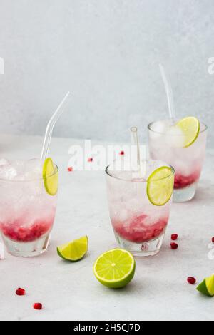 Erfrischendes Granatapfelgetränk in Gläsern mit Granatapfelkernen und Eis, Limette und Glashalmen Stockfoto