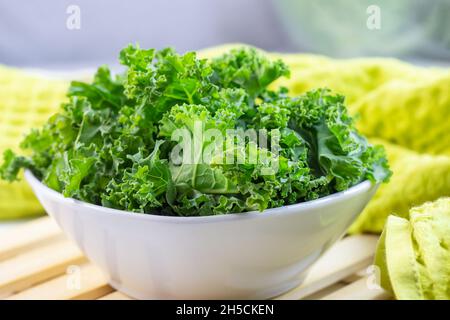 Frisches grünes Lockenkohl oder Grünkohl-Salatblätter, die auf hellem Hintergrund auf dem Tisch in der Küche in die Schüssel geschnitten werden. Stockfoto