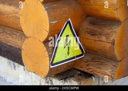 Nahaufnahme des Blockhauses. Ecke des alten Holzhauses mit gelbem Metallschild mit Bild des Blitzes befestigt, um es, Vorsicht, Gefahr Stockfoto