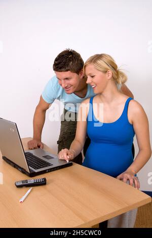 Eine Schwangere, junge Frau, die einem Mann etwas auf einem Laptop zeigt Stockfoto