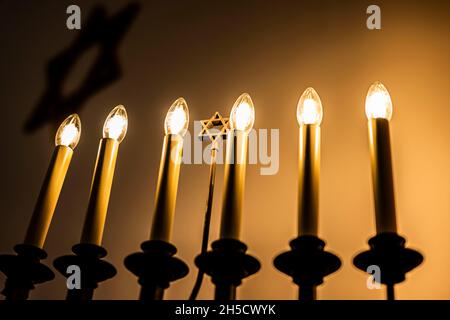 Gelsenkirchen, Deutschland. November 2021. Ein siebenarmiger Leuchter (Menorah) mit einem Davidstern in der Mitte leuchtet im Gebetsraum der Neuen Synagoge. Der 9. November 1938 ging als Tag der nationalsozialistischen Pogrome in die Geschichte ein und steht für die Verfolgung und Vernichtung der Juden. Kredit: David Inderlied/dpa/Alamy Live Nachrichten Stockfoto