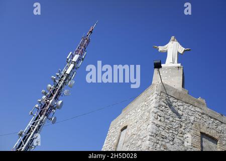 Turm mit digitaler und terrestrischer Kommunikationsantenne, neben einer religiösen Statue auf einem Berg. Stockfoto