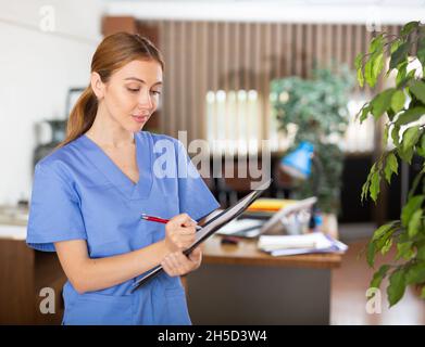 Die junge Therapeutin schreibt Notizen auf eine Tablette und steht in einem Büro Stockfoto