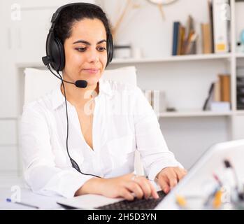 Lächelnde Sprecherin, die mit dem Kunden über das Headset im Büro des Unternehmens spricht Stockfoto
