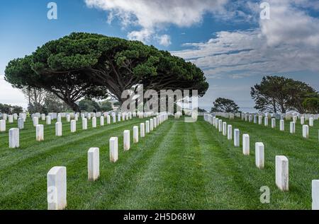 San Diego, Kalifornien, USA - 5. Oktober 2021: Fort Rosecrans National Cemetery. Gerade Linien von weißen Grabsteinen auf grünem Gras unter blauem Wolkenstein Stockfoto