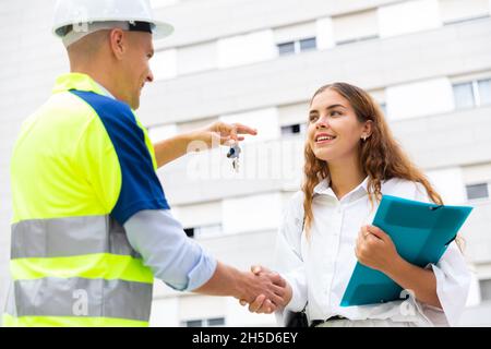 Baumeister gibt der Frau auf der Baustelle Schlüssel Stockfoto