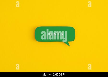 Sprechblase aus Papier mit den Worten „Join US“ auf gelbem Hintergrund. Draufsicht mit Kopierbereich. Flach liegend. Stockfoto