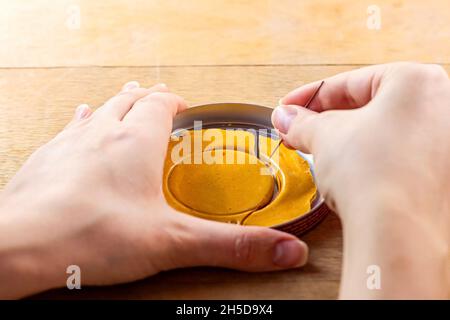 Die südkoreanische Squid Game Honeycomb Candy Herausforderung mit Dalgona Zucker Kreis Cookies in den Händen und Nadel auf Holzhintergrund. Stockfoto