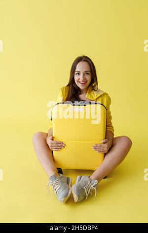 Fröhliche junge Frau mit Reisetasche im Studio sitzen Stockfoto