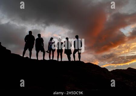 Eine Gruppe von silhouettierten Freunden genießt den orangefarbenen Sonnenuntergang in Costa Rica. Stockfoto