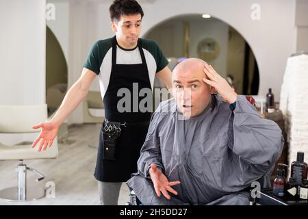 Unzufriedener Mann mit rasierten Kopf im Friseurladen Stockfoto