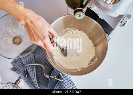 Frau gießt Olivenöl in eine Rührschüssel aus Stahl. Kochen hausgemachten Kuchen. Moderne Küchengeräte Stockfoto