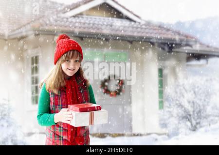 Kind im roten Hut spielt in den Weihnachtsferien im Schnee. Weihnachtsgeschenk bei einem Familienbesuch. Winterspaß im Freien. Kinder spielen im verschneiten Park. Kleines Mädchen Stockfoto