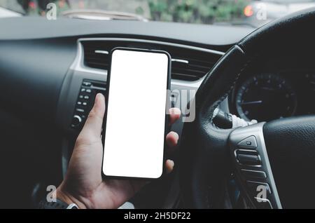 Fahrer hält ein Handy in einem Mockup Auto mit einem weißen leeren Bildschirm. Ein Mann, der ein Smartphone beobachtet, sucht nach GPS-Navigationsdaten Stockfoto