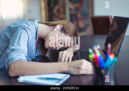 Junge, müde kaukasische Geschäftsfrau, die im Heimbüro auf dem Schreibtisch schläft Stockfoto