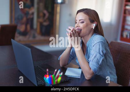 Glückliche junge kaukasische Geschäftsfrau, die im Heimbüro über den Laptop lacht, die Augen geschlossen Stockfoto