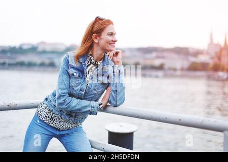 Glückliche junge Rothaarige kaukasische Frau, die am Flussufer lächelt, Profilansicht Stockfoto