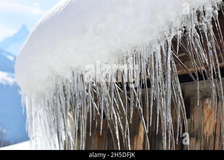 Nahaufnahme auf einem Dach eines Holzhauses, das mit Schnee und Eiszapfen bedeckt ist Stockfoto