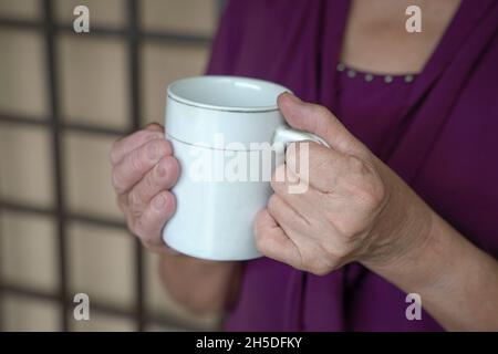 Eine ältere Frau hält eine Tasse heißen Kaffeegetränks in den Händen. Nahaufnahme. Stockfoto