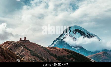 Schöner Blick auf die Dreifaltigkeitskirche oder die Dreifaltigkeitskirche Gergeti über den Kazbek-Berg. Blick von der Stadt Stepantsminda Stockfoto