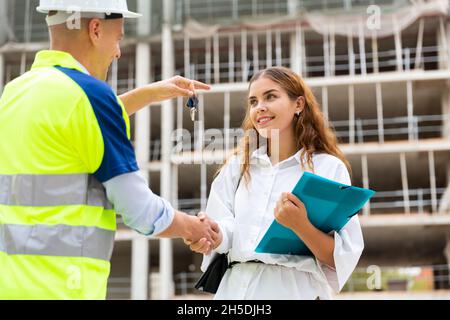 Baumeister gibt der Frau auf der Baustelle Schlüssel Stockfoto