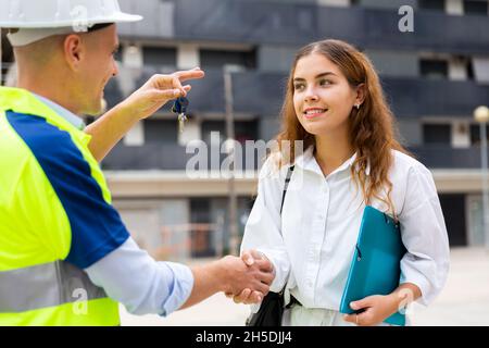 Baumeister gibt der Frau auf der Baustelle Schlüssel Stockfoto