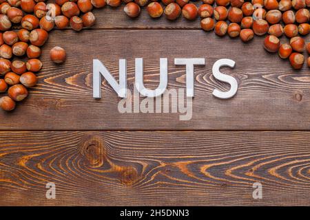 Das Wort Nüsse mit silbernen Buchstaben auf Holzbrett Hintergrund mit Haselnüssen umgeben gelegt Stockfoto