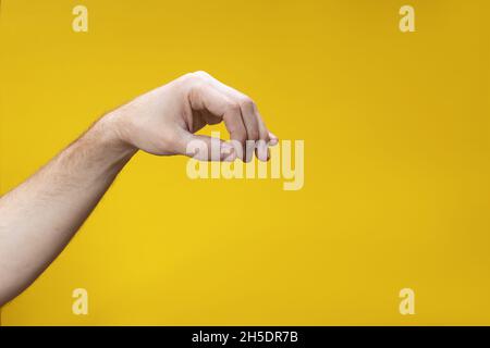 Nahaufnahme der Handbewegung, um etwas zu nehmen. Männliche Hand hält etwas Unsichtbares isoliert auf gelbem Hintergrund. Stockfoto