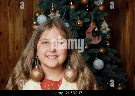 Junge glücklich lustig lächelnd langhaarige Mädchen auf geschmückten Weihnachtsbaum Hintergrund.. Mädchen an Weihnachten. Rustikales Konzept. Humor. Stockfoto